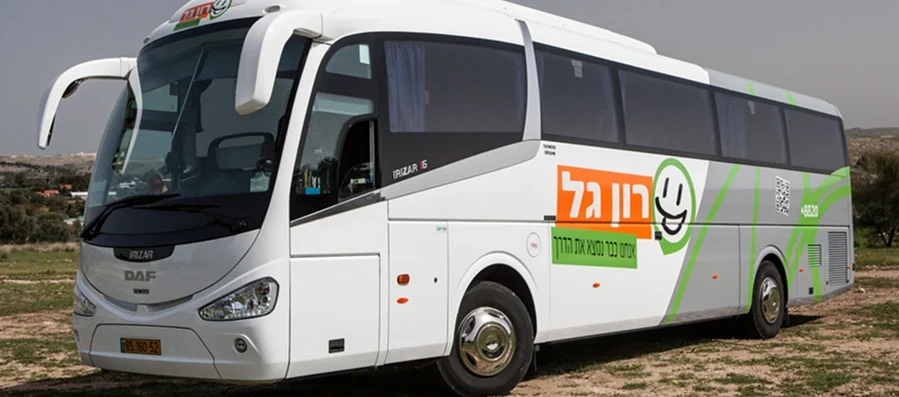 אוטובוס תיירים לבן וירוק של רון גאל חונה על הדשא, כשברקע נוף כפרי.