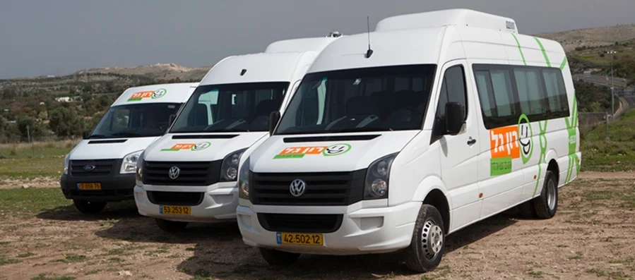 שלוש מכוניות נוסעים לבנות עם לוגו כתום וירוק חונות זו לצד זו על משטח עפר, עם נוף דשא ברקע.
